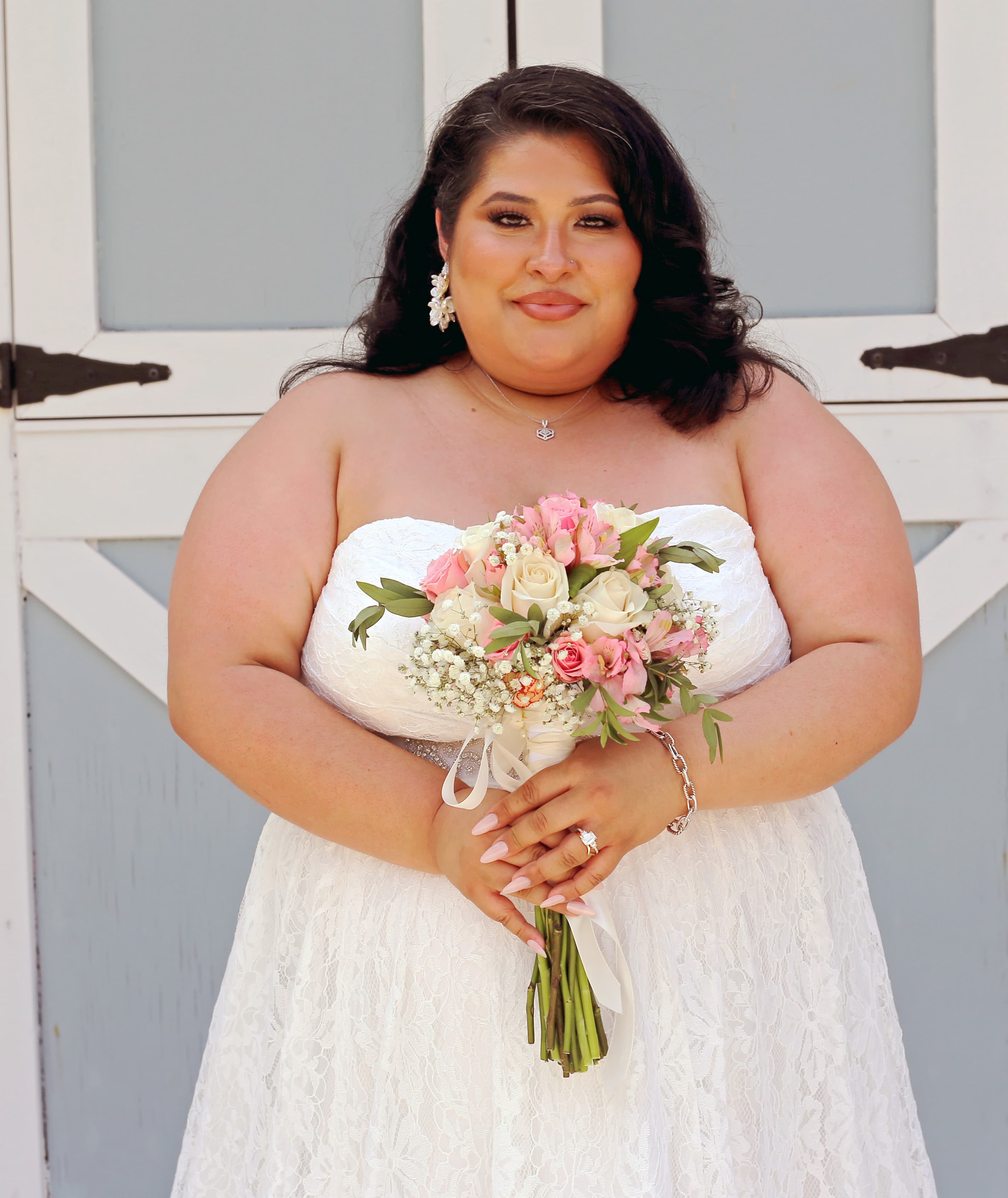 Smiling bride in a strapless lace wedding dress holding a pink and white floral bouquet.